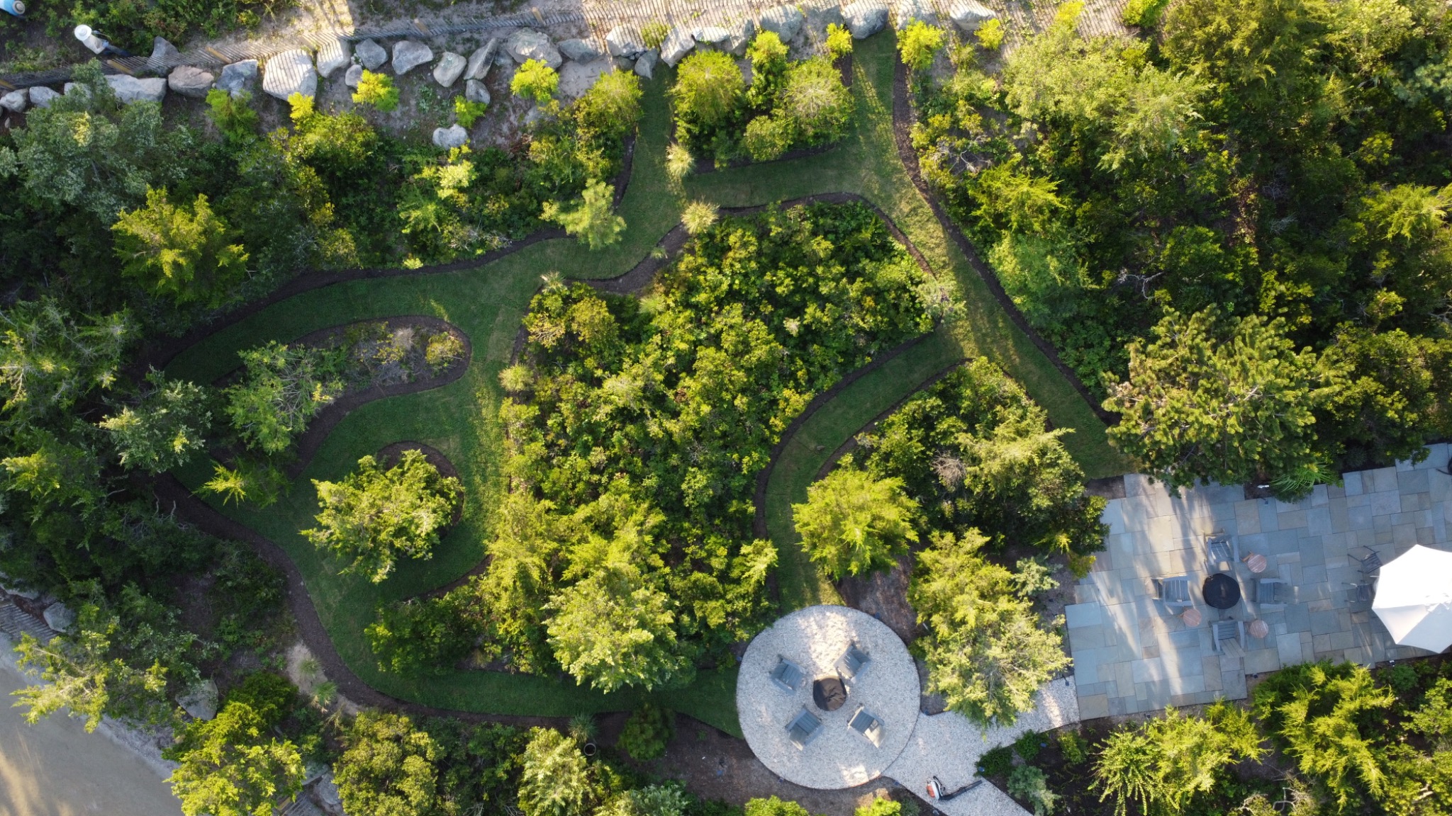 Winding grass paths through coastal planting, a circular fire pit seating area, and a bluestone patio.