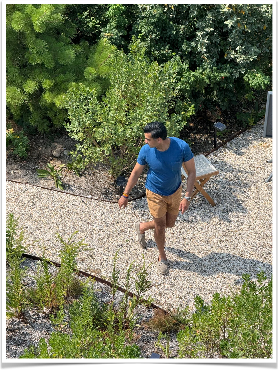 A person walking along a sunlit gravel path through the Surf House gardens