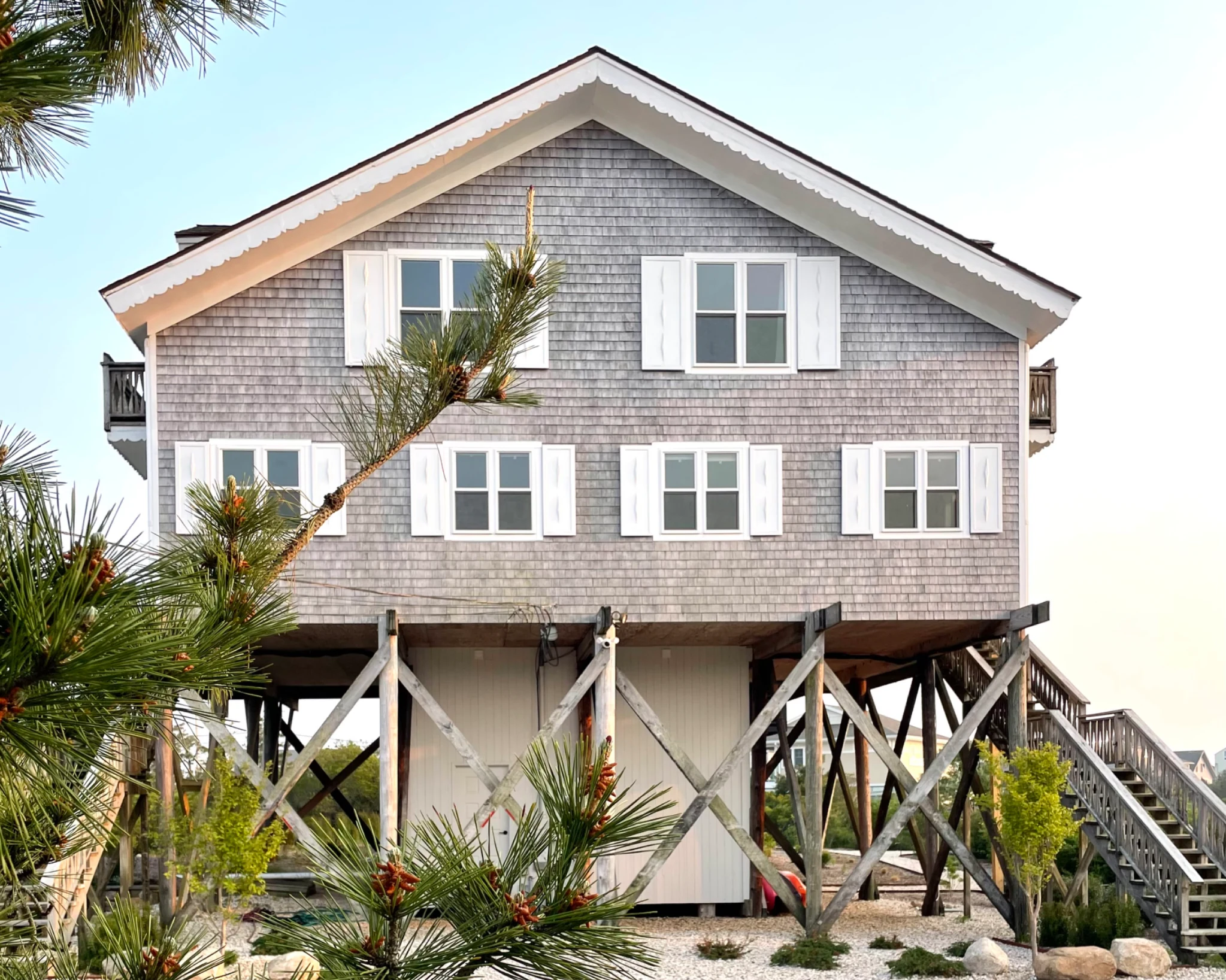 Surf House's gray shingles, white shutters, and gabled roof framed by sunlit pine branches